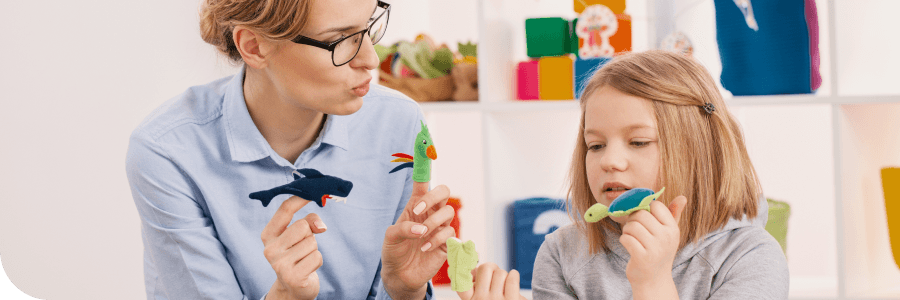 A woman and a young girl sitting at a table, playing with colorful clay models of animals in a brightly colored playroom.