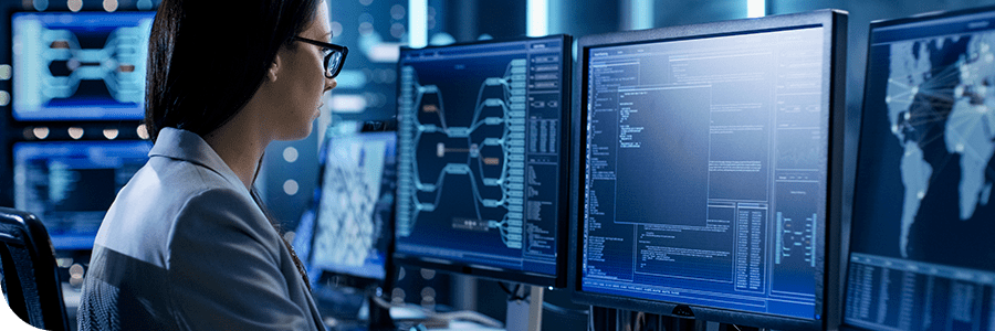 A female professional examines data on multiple computer screens in a high-tech cybersecurity control room environment.
