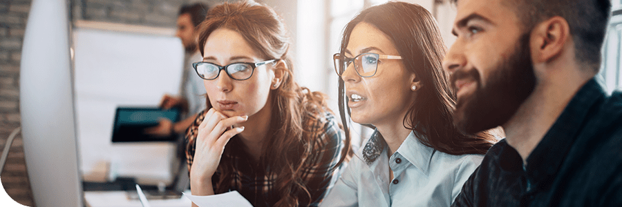 Three professionals, two women and one man, collaborate and look intently at a computer screen while discussing Online Project Management MBA programs in a modern office setting.