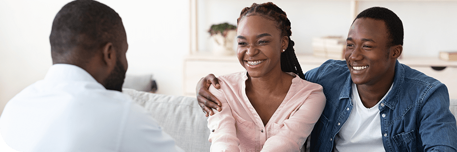 A happy African American couple meeting with a financial advisor in a bright office setting, discussing documents and smiling.