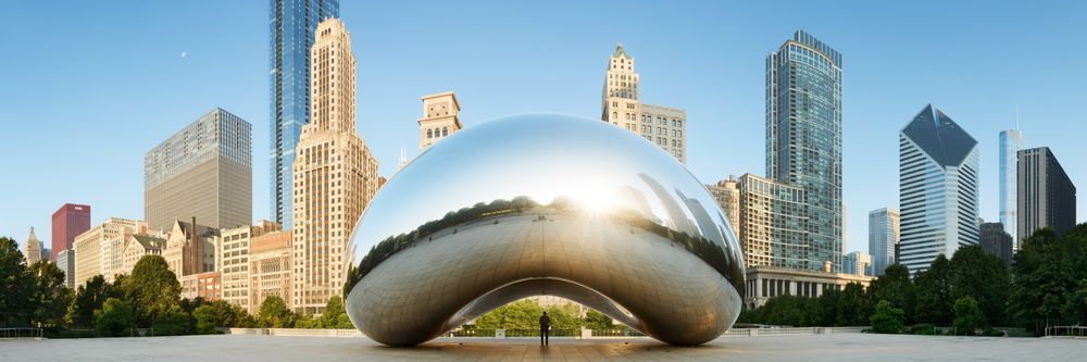 Panoramic view of cloud gate, also known as "the bean," a mirrored sculpture reflecting chicago's skyline, set against a clear blue sky in millennium park.