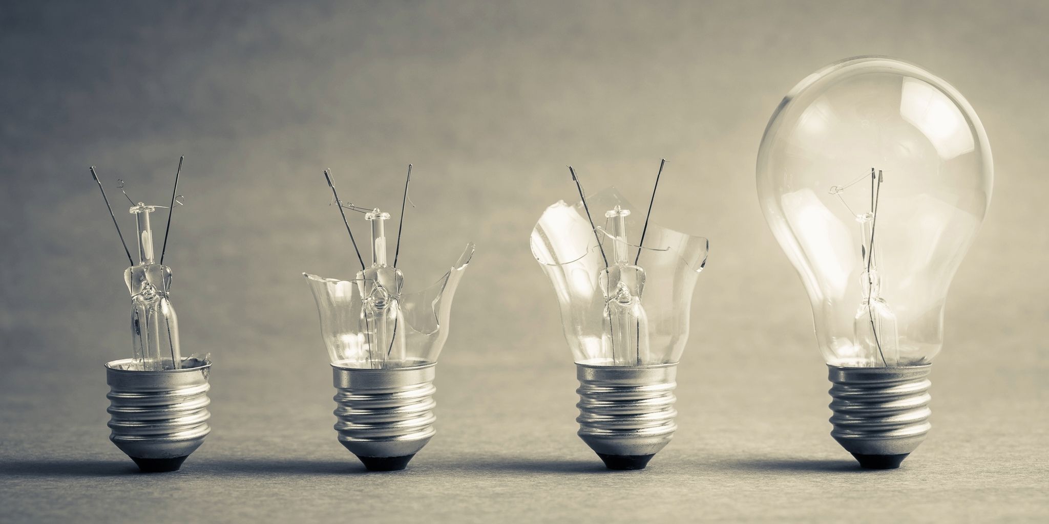 Four light bulbs in a row, with the first three progressively more broken and the last one intact, against a neutral background. The image conveys a concept of evolution, progress, or innovation.