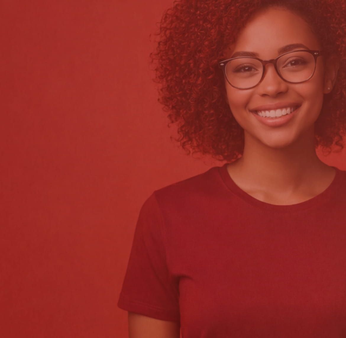 A young woman with curly hair and glasses smiles at the camera, wearing a red t-shirt, standing against a red background.